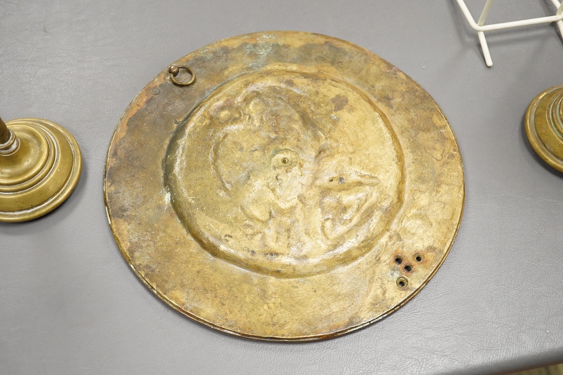 A pair of Pugin style ‘gothic’ brass candlesticks - 21cm high and a circular brass disc depicting Hercules and The Nemean Lion - 25cm in diameter